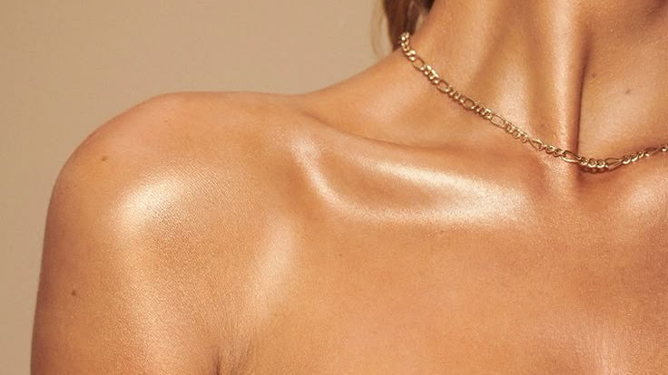 Close-up of a person wearing a gold necklace against a beige background